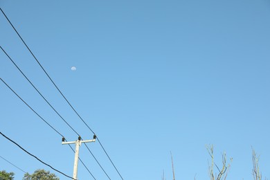 Photo of Electricity pole and wires against blue sky with moon, low angle view