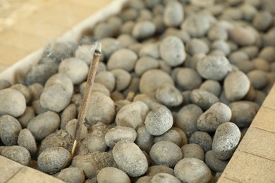 Photo of Burning incense stick in rocks indoors, closeup