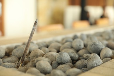 Photo of Burning incense stick in rocks indoors, closeup