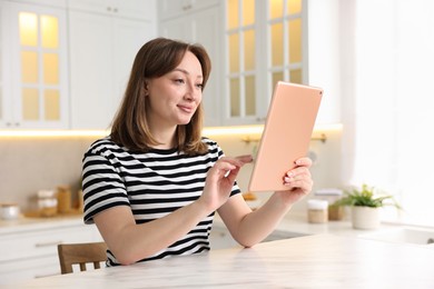 Photo of Woman with modern tablet at white marble table in kitchen