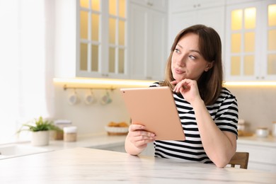 Photo of Woman with modern tablet at white marble table in kitchen, space for text