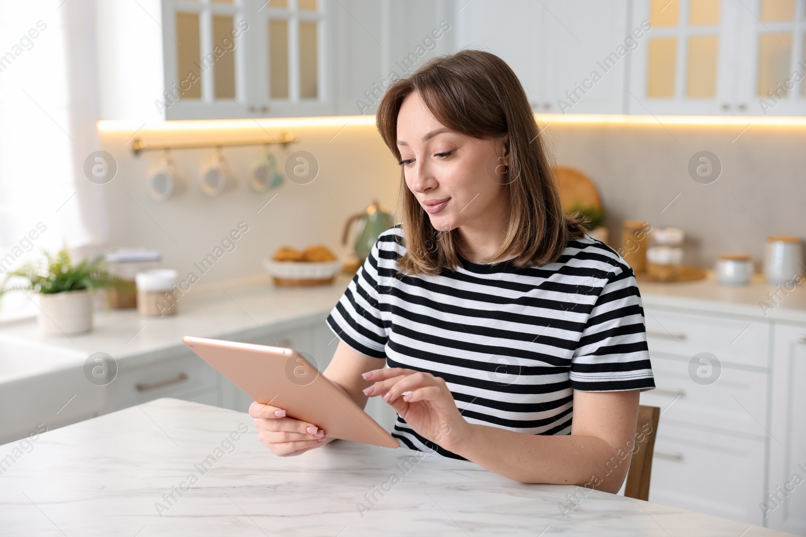 Woman with modern tablet at white marble table in kitchen Photo of Woman with modern tablet at white marble table in kitchen