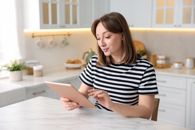 Photo of Woman with modern tablet at white marble table in kitchen