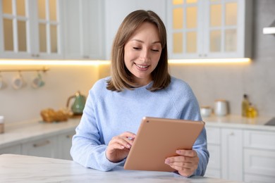 Photo of Woman with modern tablet at white marble table in kitchen
