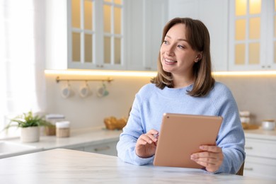 Photo of Woman with modern tablet at white marble table in kitchen, space for text