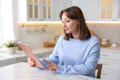 Photo of Woman with modern tablet at white marble table in kitchen