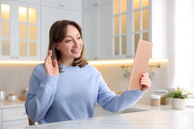 Photo of Woman having video chat via modern tablet at white marble table in kitchen