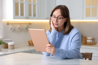 Photo of Woman with modern tablet at white marble table in kitchen, space for text