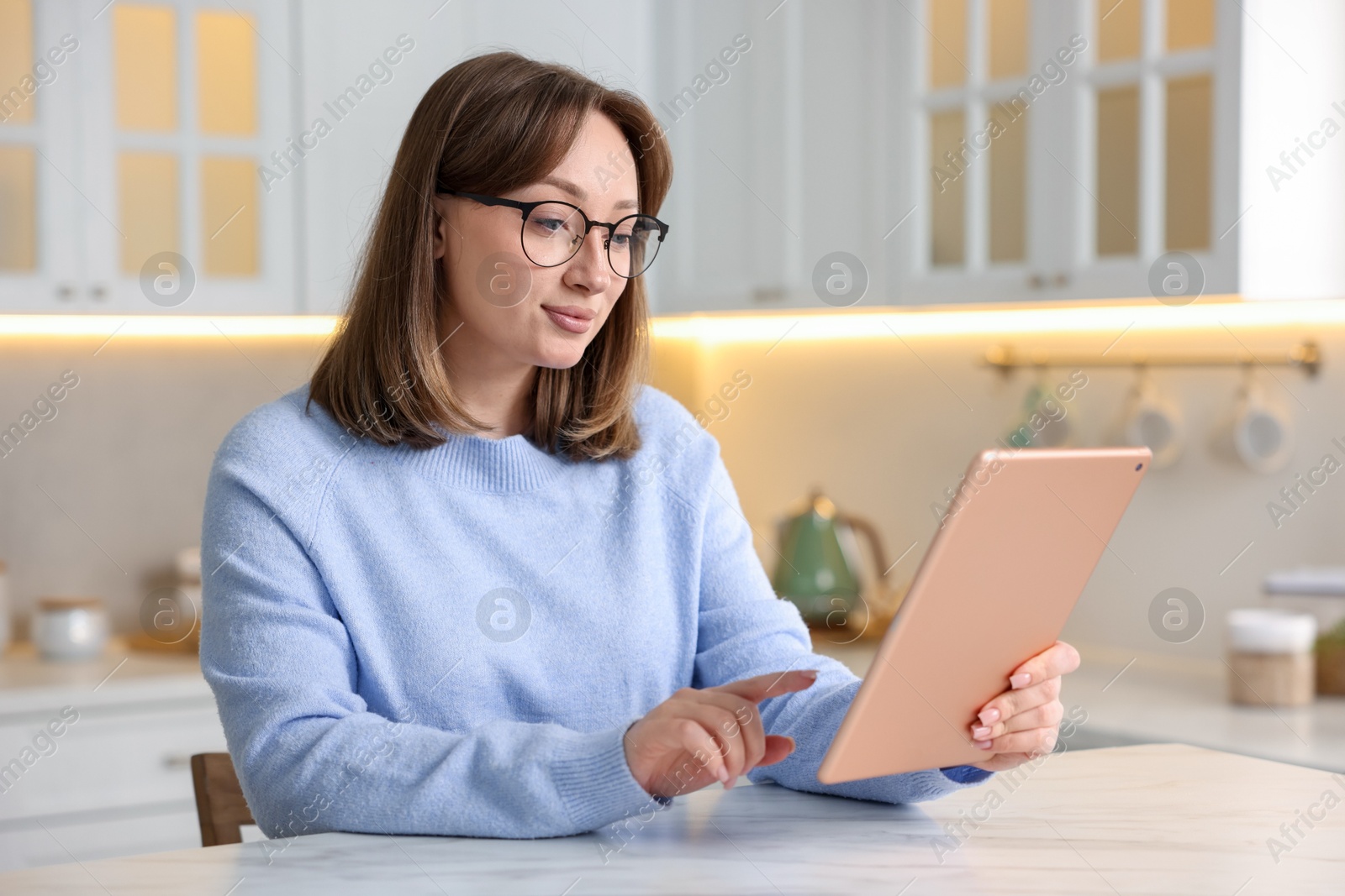 Woman with modern tablet at white marble table in kitchen Photo of Woman with modern tablet at white marble table in kitchen