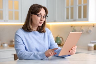 Photo of Woman with modern tablet at white marble table in kitchen