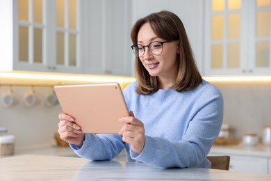 Photo of Woman with modern tablet at white marble table in kitchen
