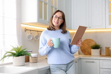 Photo of Woman with modern tablet and cup of drink in kitchen