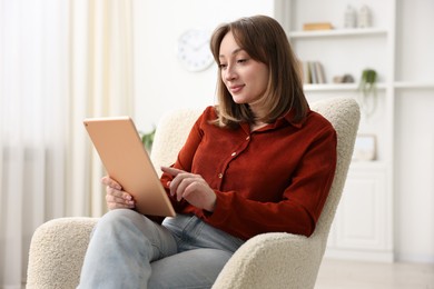 Photo of Woman with modern tablet in armchair at home