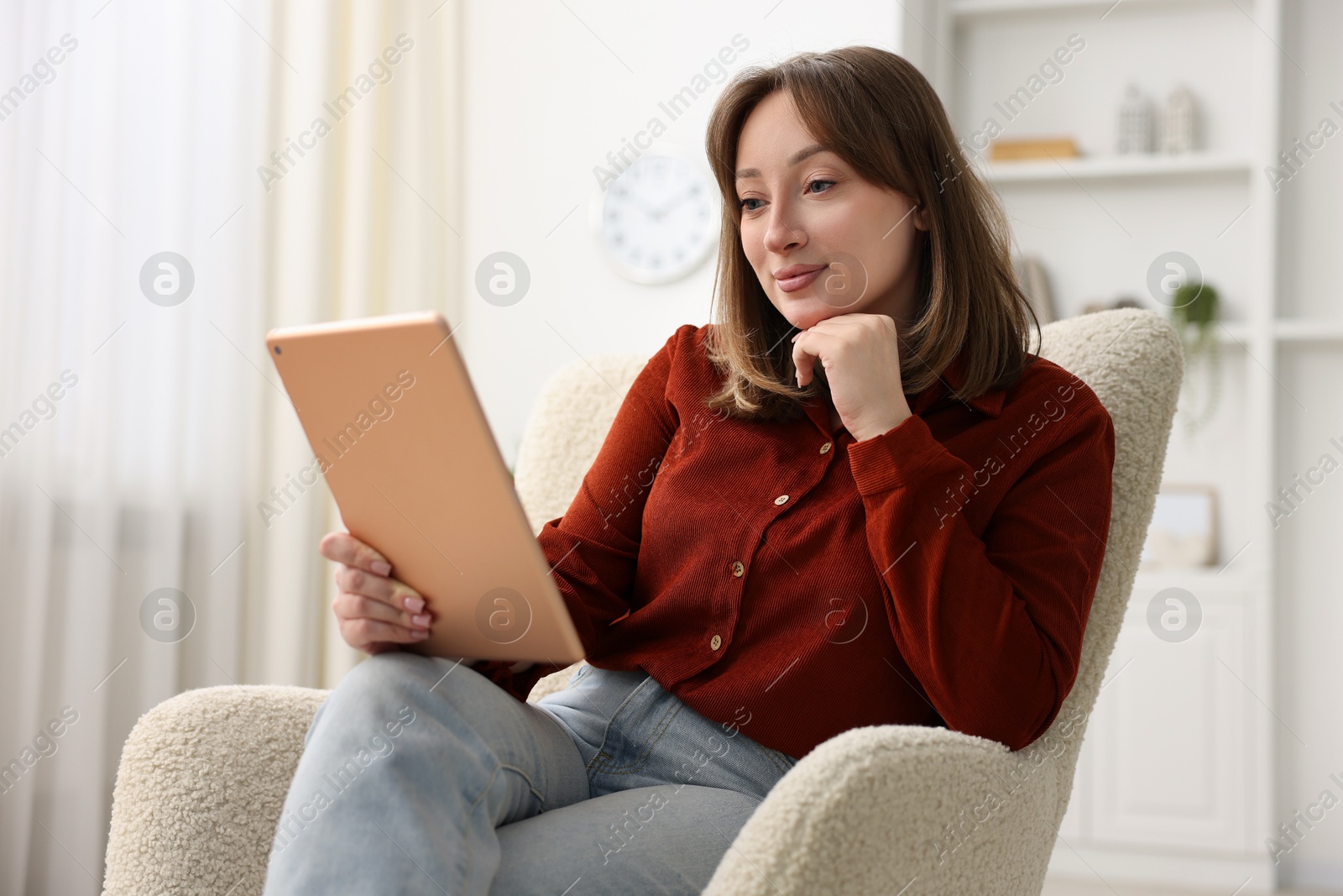 Woman with modern tablet in armchair at home Photo of Woman with modern tablet in armchair at home