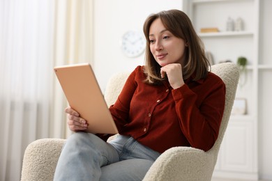 Photo of Woman with modern tablet in armchair at home