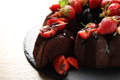 Photo of Delicious chocolate bundt cake with strawberries on wooden table, closeup