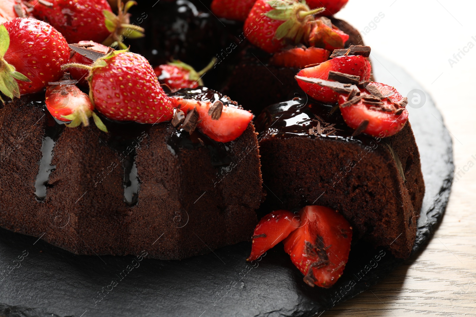 Photo of Delicious chocolate bundt cake with strawberries on wooden table, closeup