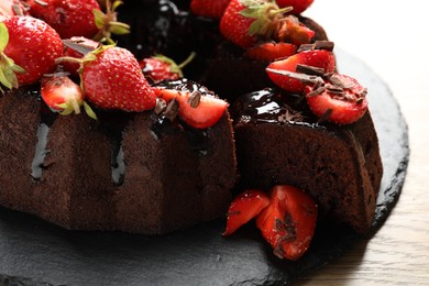 Photo of Delicious chocolate bundt cake with strawberries on wooden table, closeup