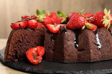 Photo of Delicious chocolate bundt cake with strawberries on wooden table, closeup