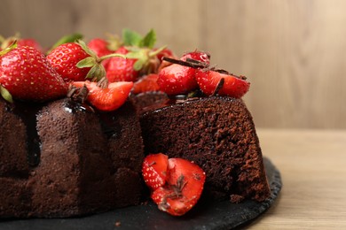 Photo of Delicious chocolate bundt cake with strawberries on wooden table, closeup