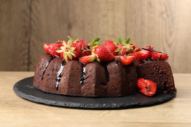 Photo of Delicious chocolate bundt cake with strawberries on wooden table, closeup