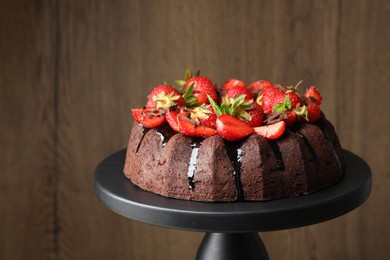 Photo of Delicious bundt cake with strawberries, mint and chocolate shavings on stand against blurred background, closeup