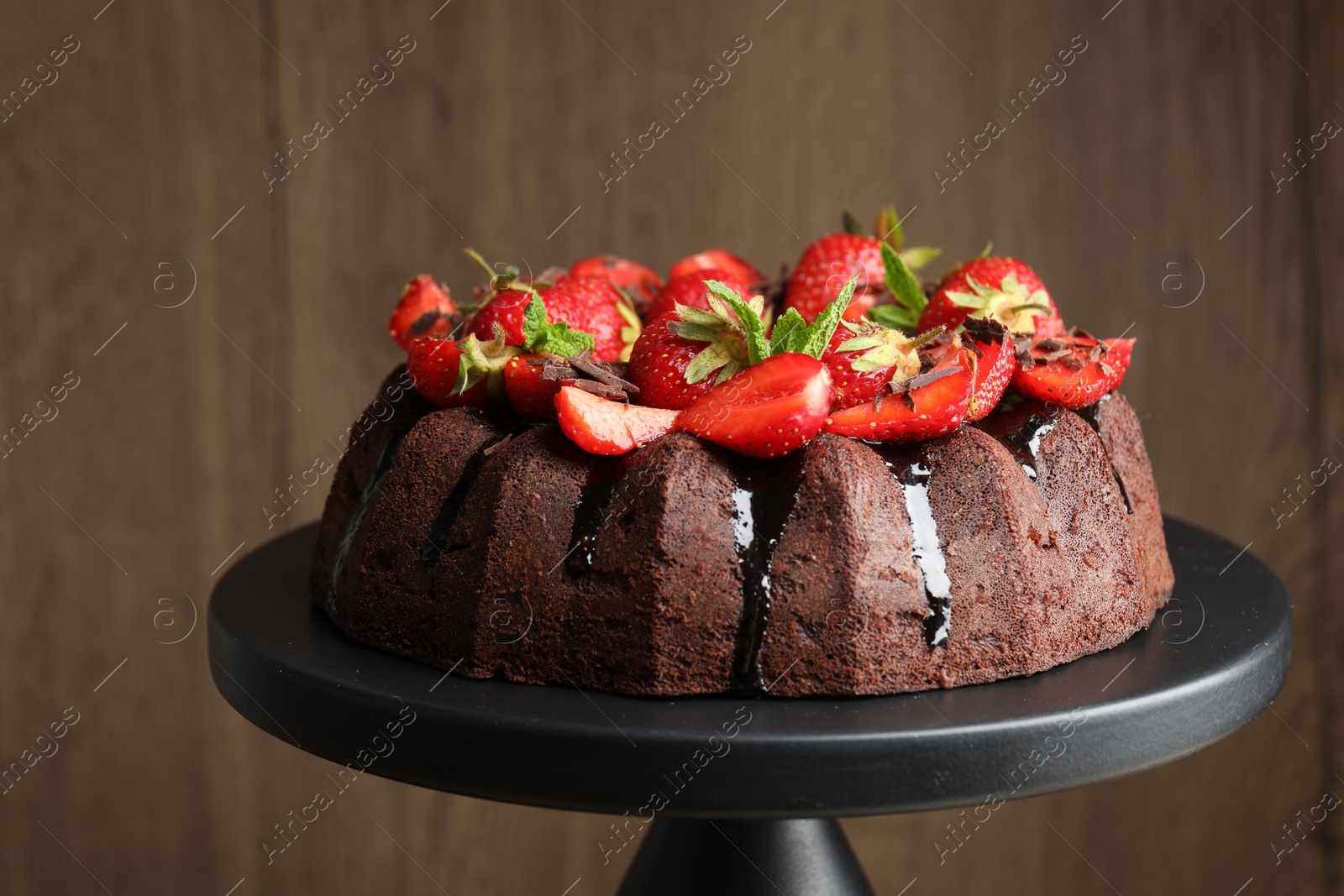 Delicious bundt cake with strawberries, mint and chocolate shavings on stand against blurred background, closeup Photo of Delicious bundt cake with strawberries, mint and chocolate shavings on stand against blurred background, closeup