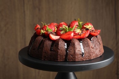 Photo of Delicious bundt cake with strawberries, mint and chocolate shavings on stand against blurred background, closeup