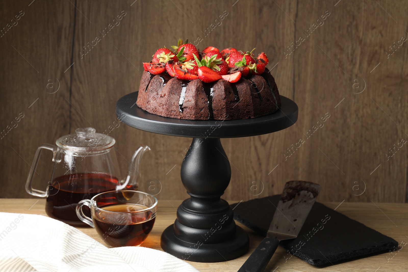 Delicious chocolate bundt cake with strawberries and tea on wooden table Photo of Delicious chocolate bundt cake with strawberries and tea on wooden table