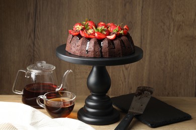 Photo of Delicious chocolate bundt cake with strawberries and tea on wooden table