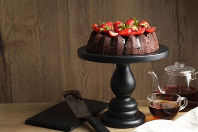 Photo of Delicious chocolate bundt cake with strawberries and tea on wooden table