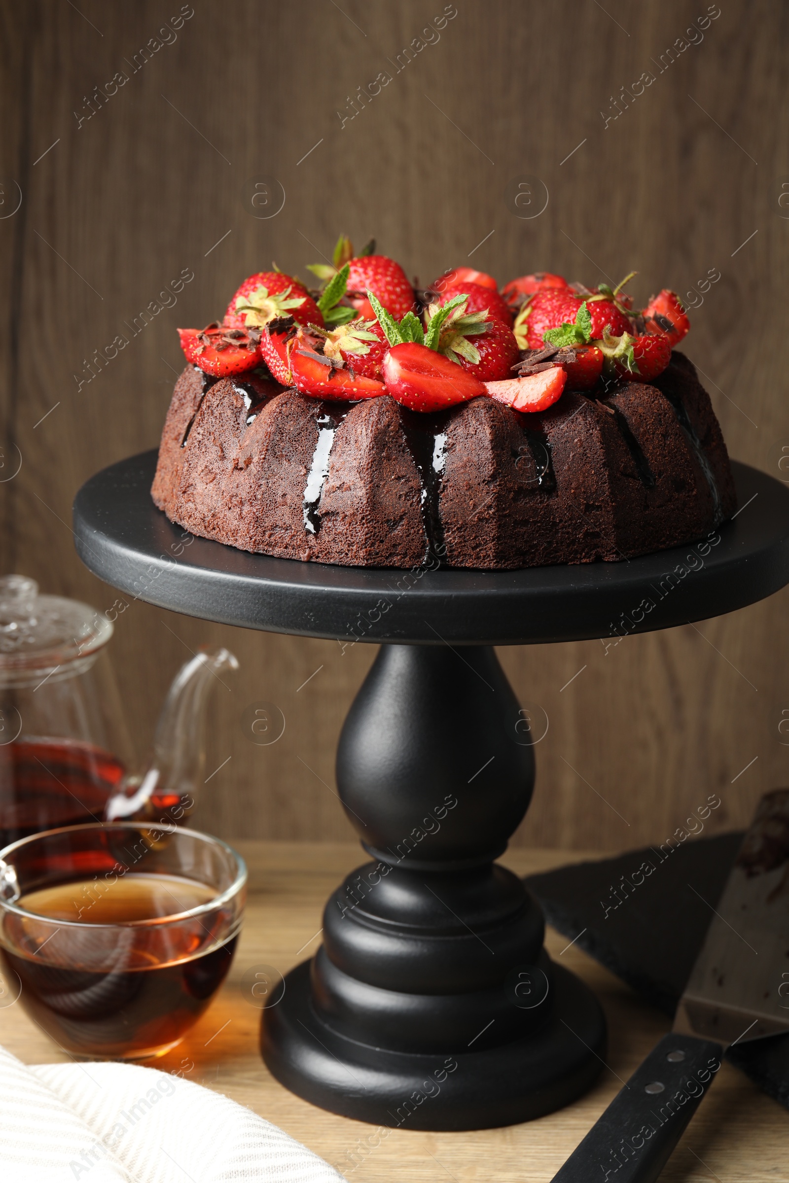Delicious chocolate bundt cake with strawberries and tea on wooden table, closeup Photo of Delicious chocolate bundt cake with strawberries and tea on wooden table, closeup
