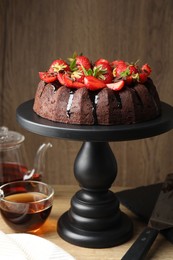 Photo of Delicious chocolate bundt cake with strawberries and tea on wooden table, closeup