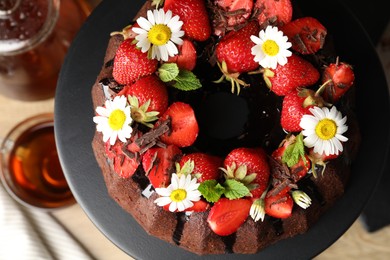 Photo of Delicious chocolate bundt cake with strawberries, mint and chamomile flowers on table, top view