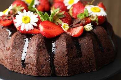 Photo of Delicious chocolate bundt cake with strawberries, chamomile flowers and mint on stand, closeup