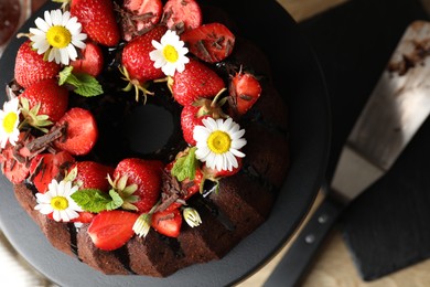 Photo of Delicious chocolate bundt cake with strawberries, mint and chamomile flowers on table, top view