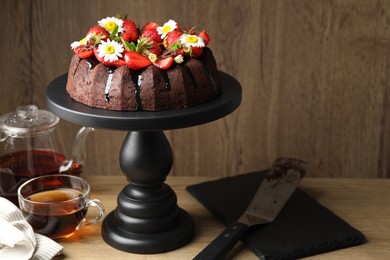 Photo of Delicious chocolate bundt cake with strawberries, chamomile flowers and tea on wooden table