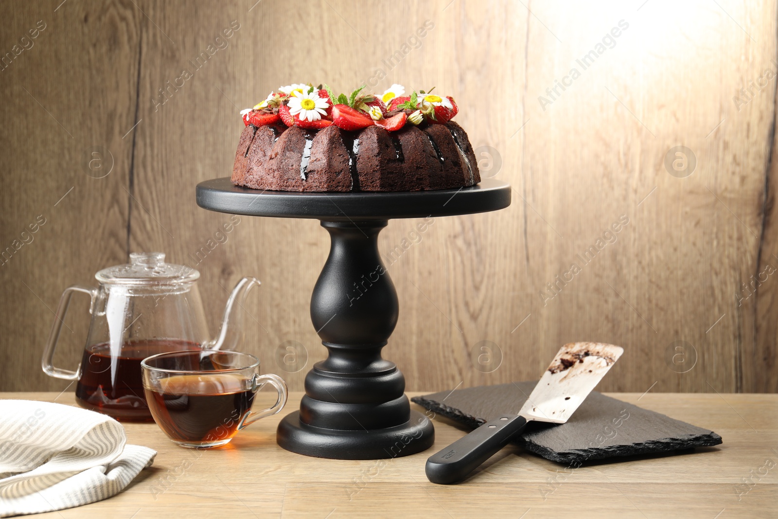 Delicious chocolate bundt cake with strawberries, chamomile flowers and tea on wooden table Photo of Delicious chocolate bundt cake with strawberries, chamomile flowers and tea on wooden table