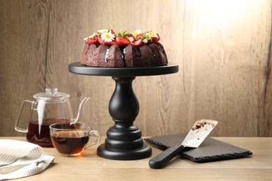 Photo of Delicious chocolate bundt cake with strawberries, chamomile flowers and tea on wooden table