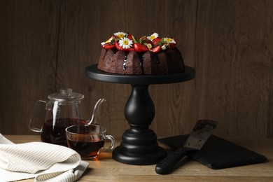 Photo of Delicious chocolate bundt cake with strawberries, chamomile flowers and tea on wooden table