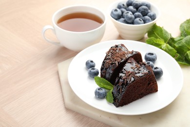 Photo of Pieces of delicious bundt cake with blueberries, mint, chocolate shavings and tea on wooden table, closeup
