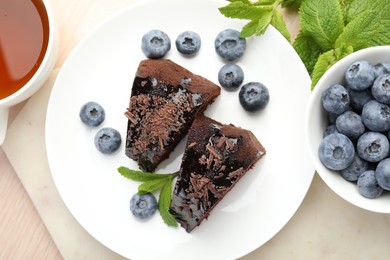 Photo of Pieces of delicious bundt cake with blueberries, mint and chocolate shavings on wooden table, flat lay