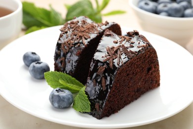 Photo of Pieces of delicious bundt cake with blueberries, mint, and chocolate shavings on table, closeup