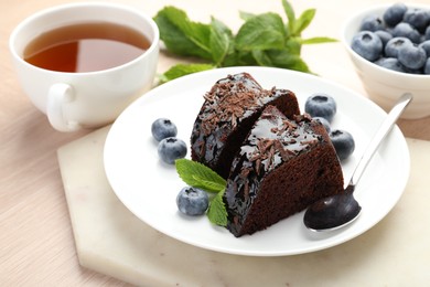 Photo of Pieces of delicious bundt cake with blueberries, mint, chocolate shavings and tea on wooden table, closeup