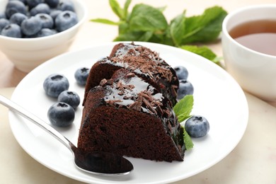 Photo of Pieces of delicious bundt cake with blueberries, mint, and chocolate shavings on table, closeup