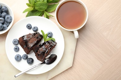 Photo of Pieces of delicious bundt cake with blueberries, mint, chocolate shavings and tea on wooden table, flat lay. Space for text