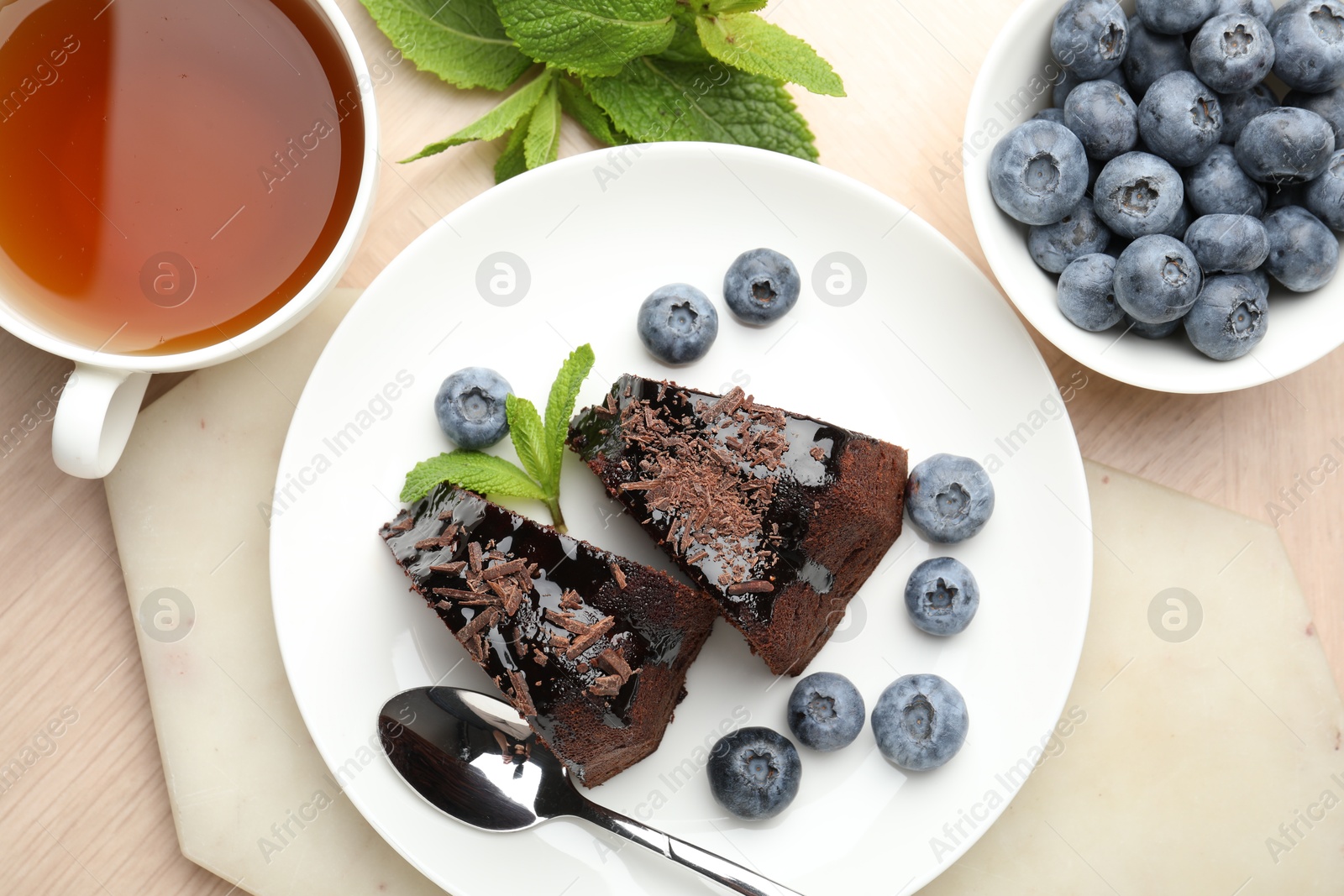 Pieces of delicious bundt cake with blueberries, mint, chocolate shavings and tea on wooden table, flat lay Photo of Pieces of delicious bundt cake with blueberries, mint, chocolate shavings and tea on wooden table, flat lay