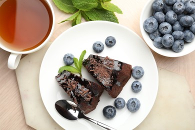Photo of Pieces of delicious bundt cake with blueberries, mint, chocolate shavings and tea on wooden table, flat lay
