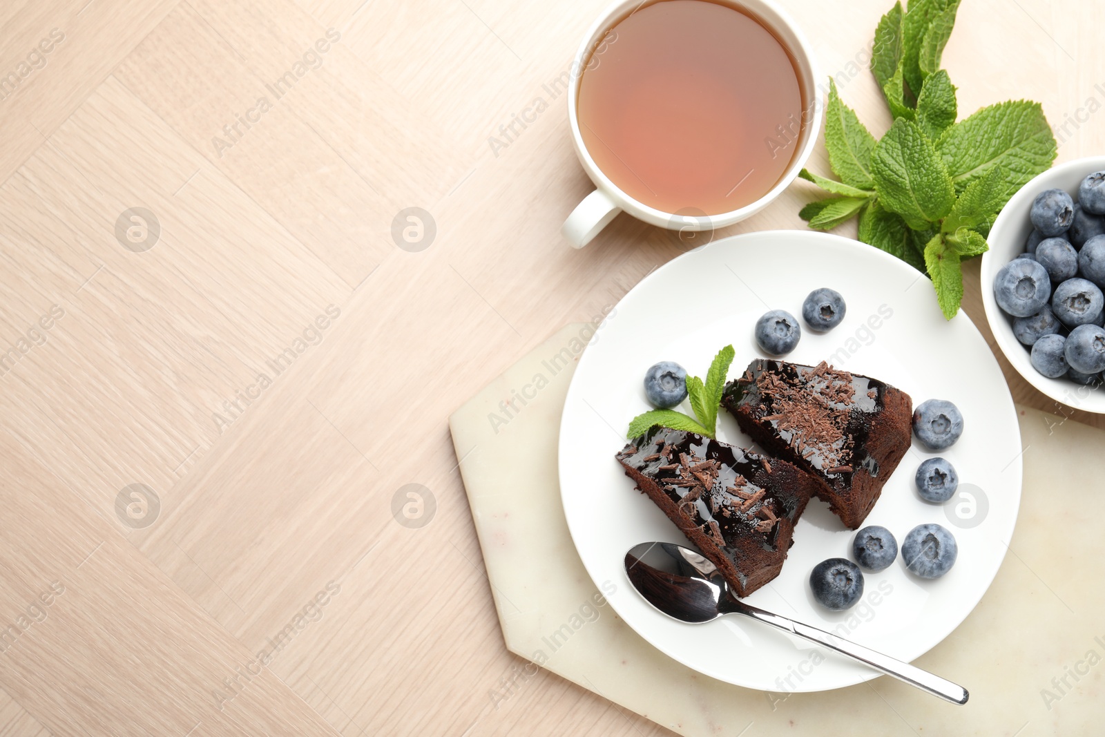 Pieces of delicious bundt cake with blueberries, mint, chocolate shavings and tea on wooden table, flat lay. Space for text Photo of Pieces of delicious bundt cake with blueberries, mint, chocolate shavings and tea on wooden table, flat lay. Space for text