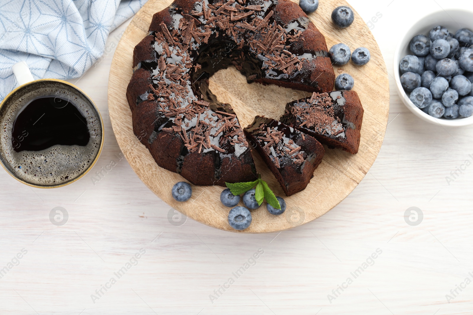 Delicious bundt cake with blueberries, mint, chocolate shavings and coffee on light wooden table, flat lay. Space for text Photo of Delicious bundt cake with blueberries, mint, chocolate shavings and coffee on light wooden table, flat lay. Space for text